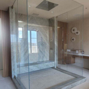 Modern glass-enclosed shower with stone flooring and walls, featuring dual doors and ceiling-mounted rainfall showerhead.