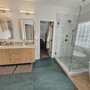 Modern bathroom with double sink vanity, glass shower, freestanding tub, and large tile flooring.